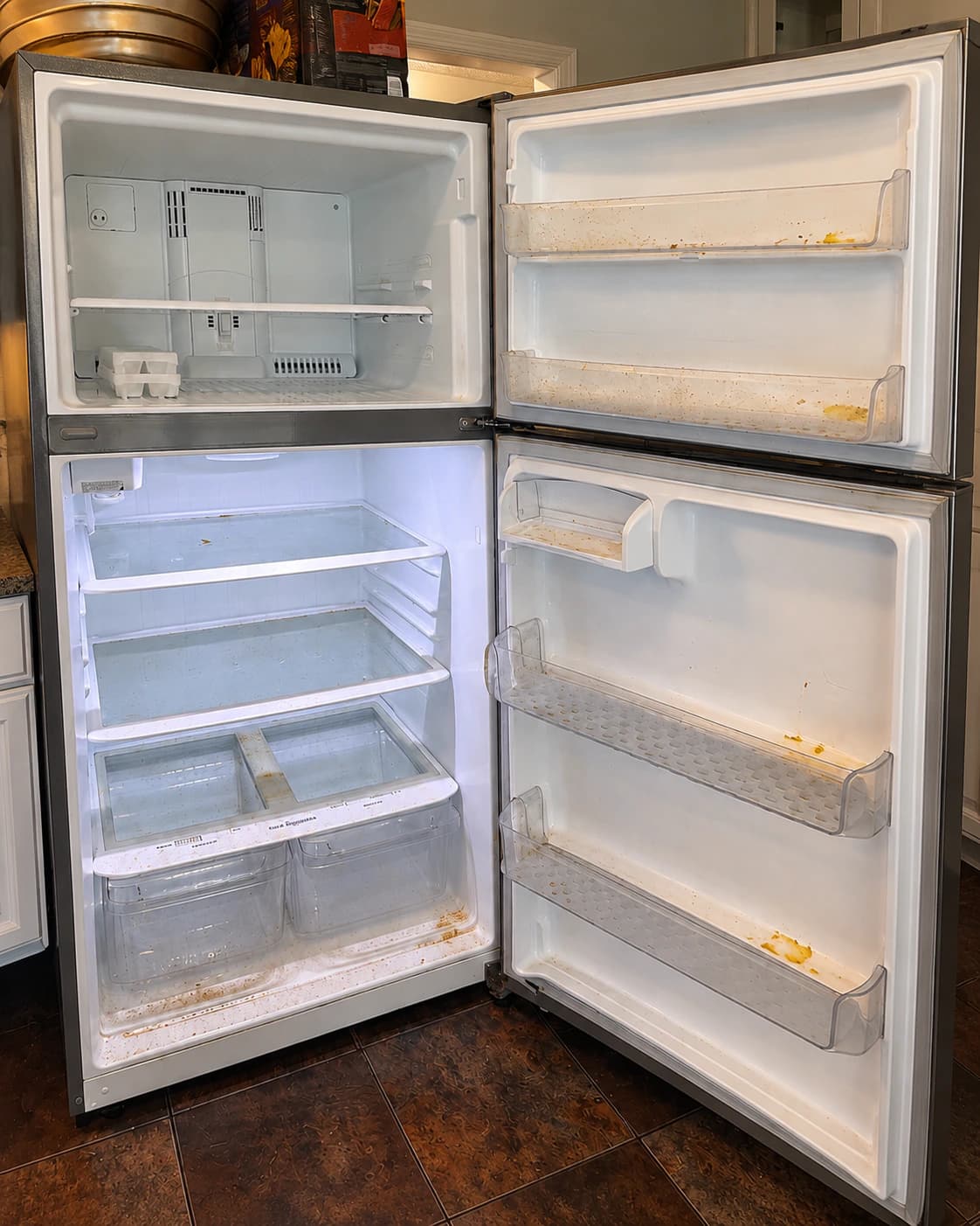 Open refrigerator before cleaning, with stains and dried residue on the shelves and in the door bins.